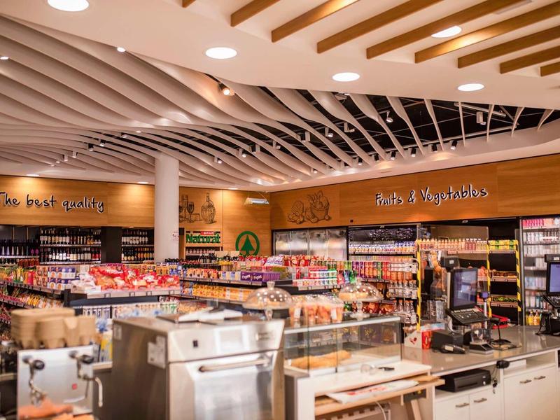 Área de compras moderna con alimentos y máquinas de café bajo luz brillante en el techo.