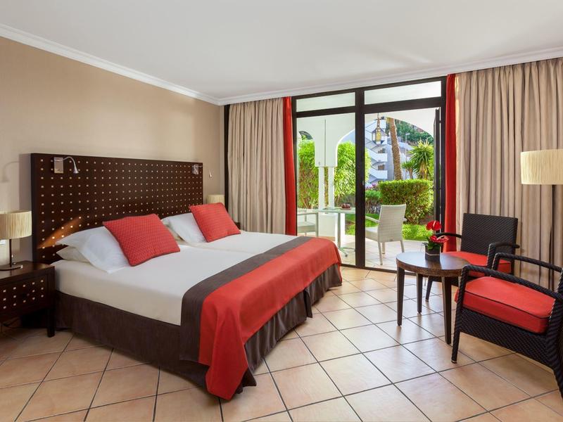 Chambre d'hôtel élégante avec lit double, coussins rouges et terrasse extérieure.