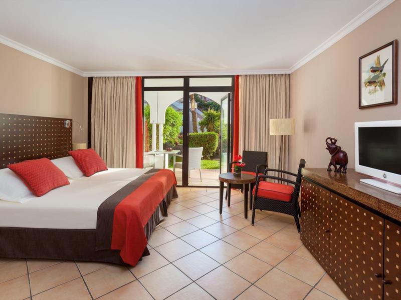 Chambre d'hôtel avec lit double, fauteuils et porte vitrée donnant sur le jardin.