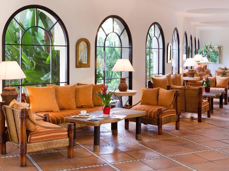 Salon d'hôtel lumineux et confortable avec fauteuils marron et grandes fenêtres en arc.