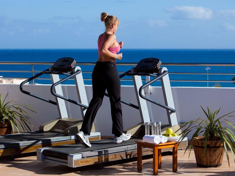 Femme courant sur un tapis roulant sur une terrasse avec vue sur la mer par ciel clair.