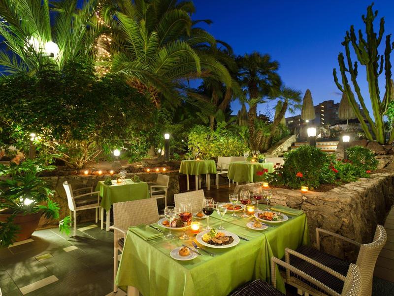 Jardin en soirée avec table dressée et plantes tropicales sur terrasse d'hôtel.