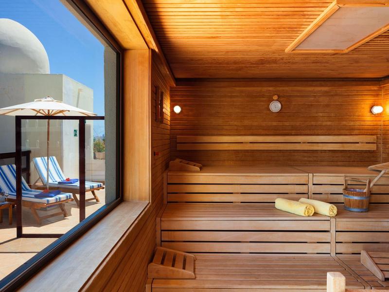 Intérieur de sauna en bois avec vue sur une terrasse ensoleillée avec chaises longues.
