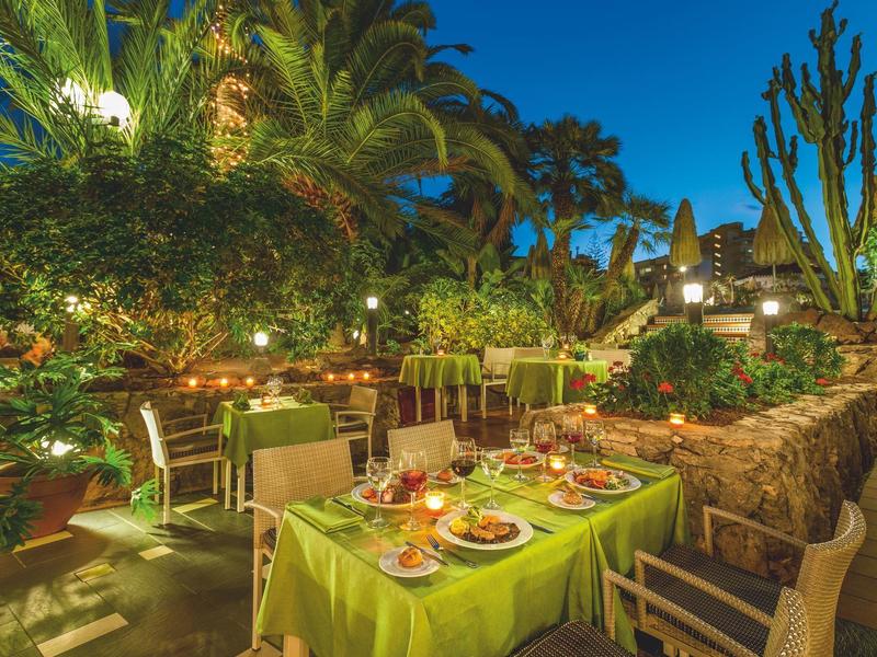 Dîner dans un jardin avec tables dressées, plantes et éclairage d'ambiance