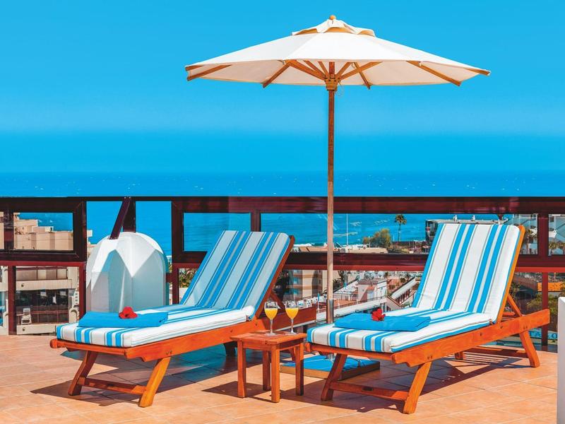 Deux chaises longues bleues avec parasol sur terrasse avec vue sur la mer.