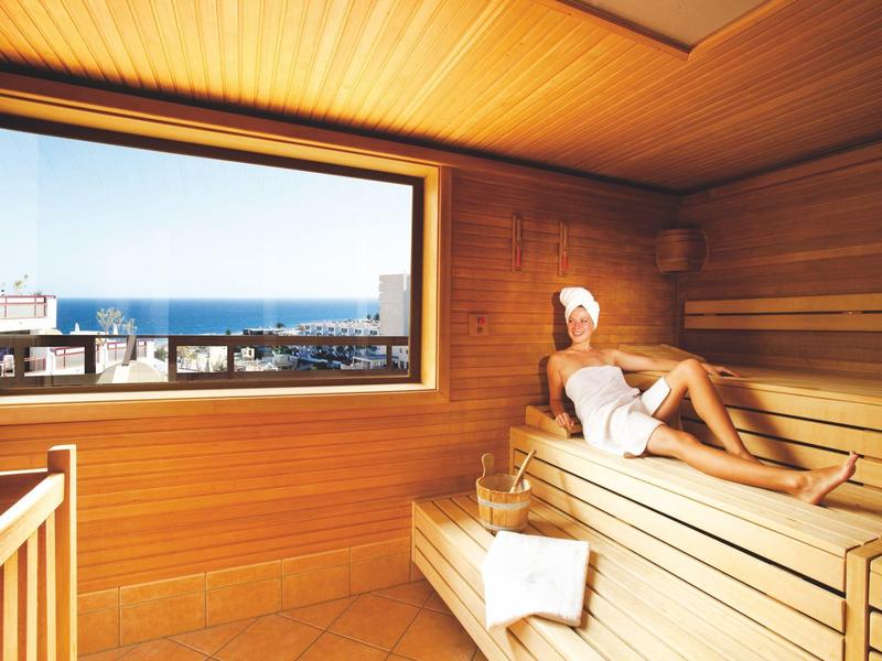 Femme se détend dans un sauna avec vue sur la ville et la mer à travers une grande fenêtre.