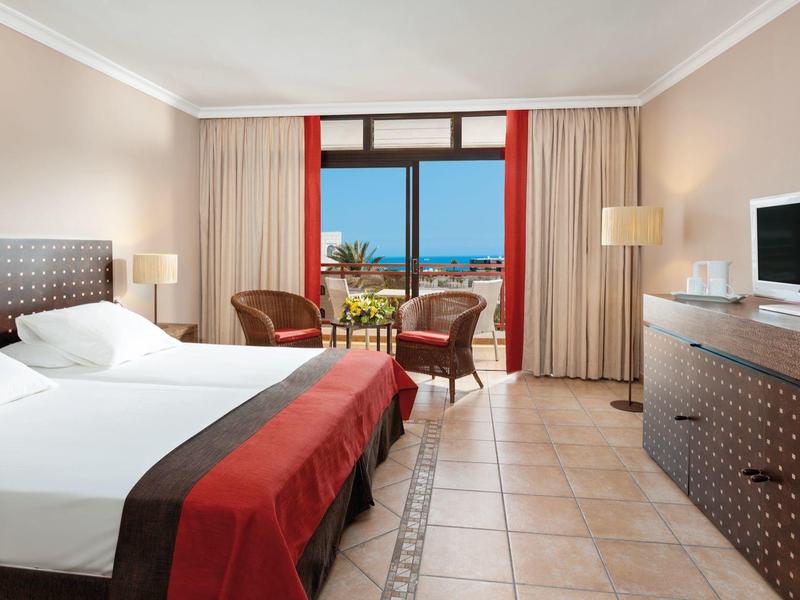 Chambre d'hôtel avec lit double, coin salon et vue sur la mer par les fenêtres