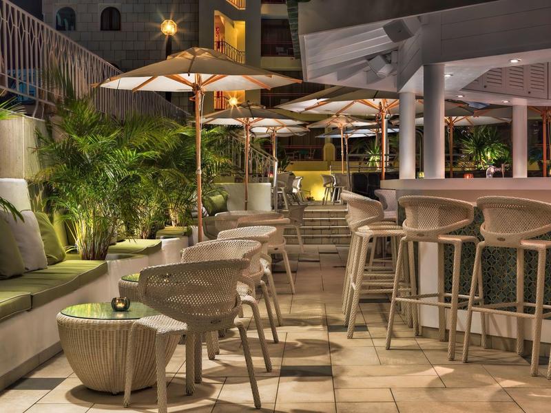 Terrasse de bar en soirée avec chaises, tables et éclairage d'ambiance dans un cadre hôtelier.
