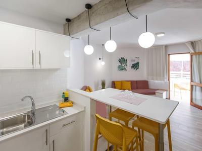 Moderner Wohnraum mit weißer Küche, Holzstühlen, Pendelleuchten und gemütlicher Sofaecke.