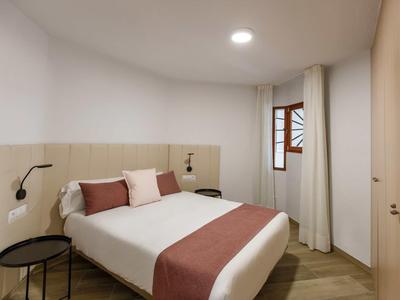 Kleines, schlicht eingerichtetes Schlafzimmer mit Doppelbett, Holzfußboden und Fenster an der Wand.