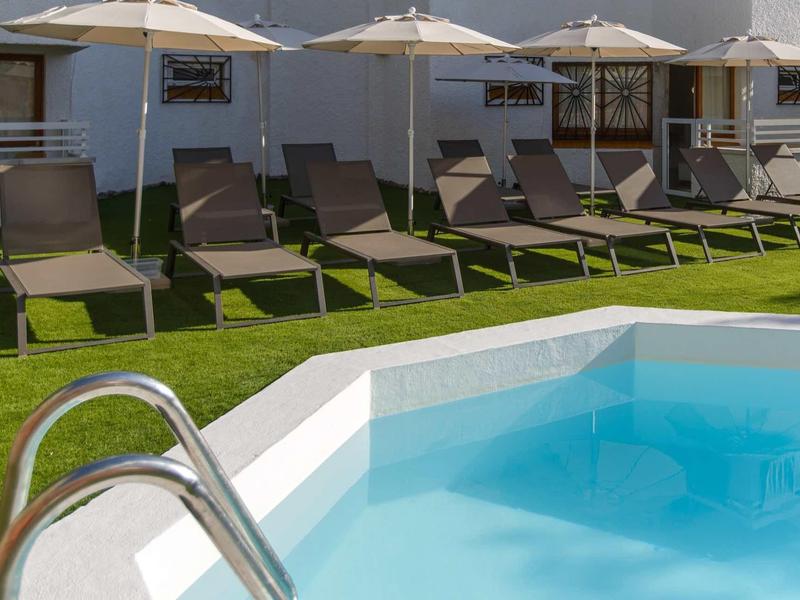 Pohled na bazén s lehátky a slunečníky na trávníku vedle hotelových budov.