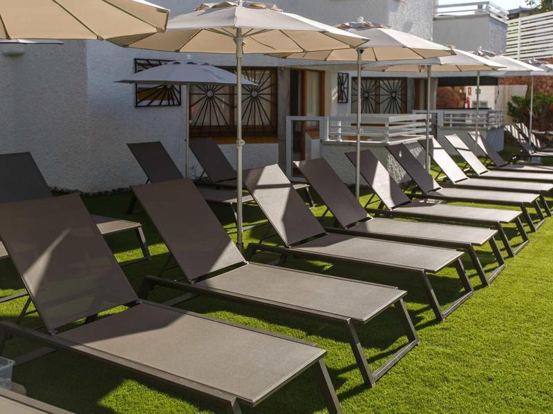 Řada lehátek se slunečníky na zeleném trávníku před hotelem