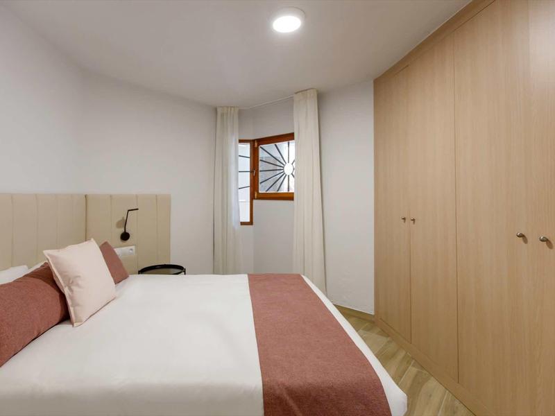 Moderní hotelový pokoj s manželskou postelí, dřevěným nábytkem a oknem se záclonou.