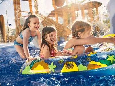 Three children happily play in the water with a swim ring on a sunny day.