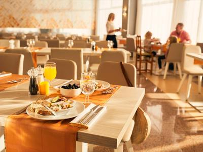 Brightly lit hotel restaurant table with breakfast and drinks in foreground.