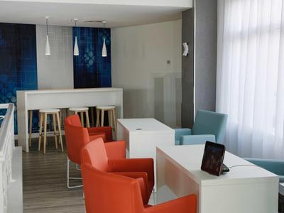 Modern hotel room with white tables, orange chairs, and large windows with curtains.