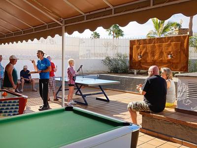 People playing and relaxing in a sunny outdoor area with a pool table and table tennis.