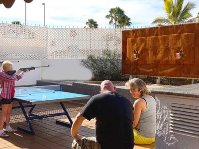 Four people outdoors playing table tennis and shooting rifles at targets.