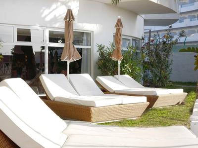 Three white lounge chairs with umbrellas on green grass next to a white building.