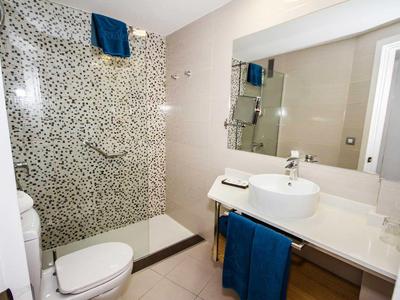 Bright bathroom with mosaic shower, white sink, and blue towels.