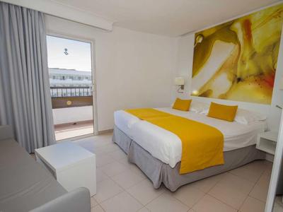 Modern hotel room with double bed, yellow accents, and balcony access with sea view.