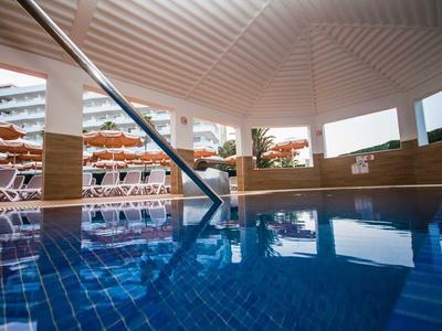 Covered swimming pool with blue tiles and view of outdoor lounge chairs.