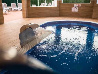 Indoor pool with waterfall and calm blue water, surrounded by wood paneling.