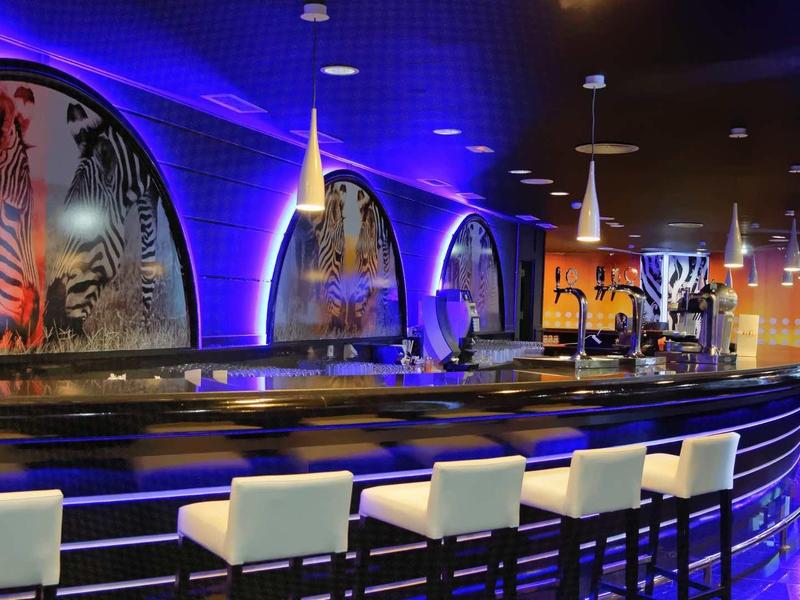 Modern hotel bar with blue lighting, white stools, and zebra patterns on the walls.