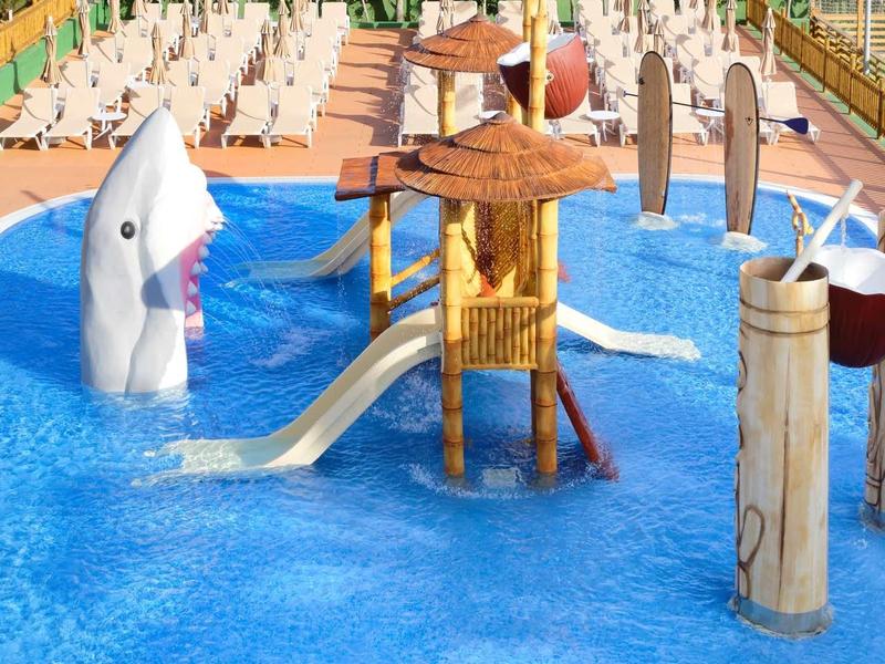 Colorful children's splash pool with water play structures and slide outdoors at a hotel.