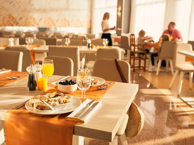 Brightly lit hotel restaurant table with breakfast and drinks in foreground.