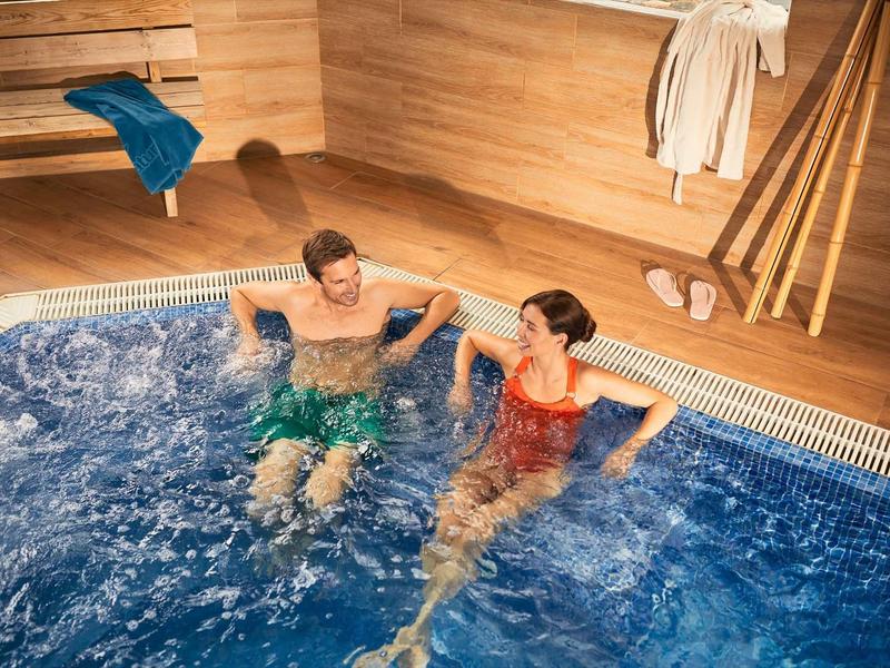 A couple relaxes in a hot tub in a luxurious spa with wooden paneling.
