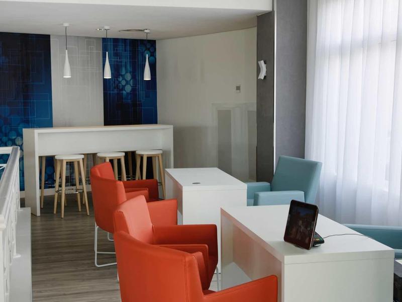 Modern hotel room with white tables, orange chairs, and large windows with curtains.