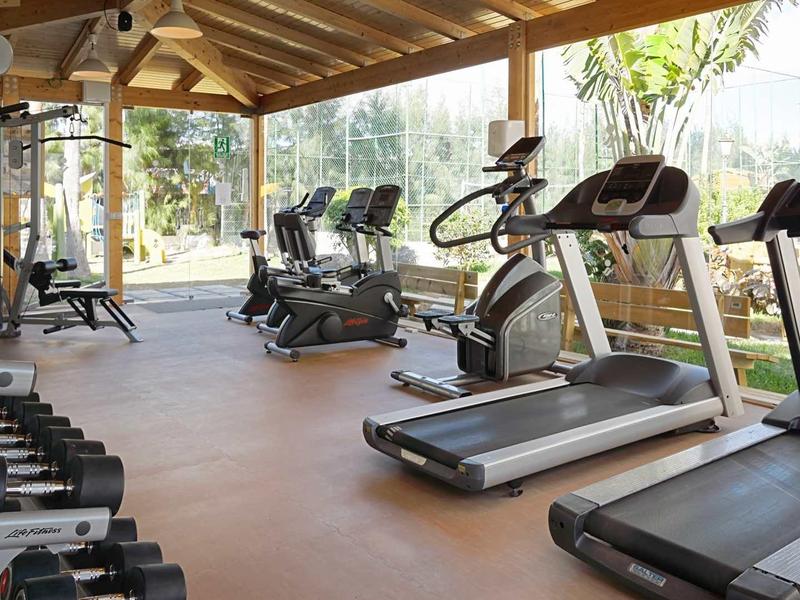 Gym with treadmills, bikes, and dumbbells by large windows and wooden beam ceiling.