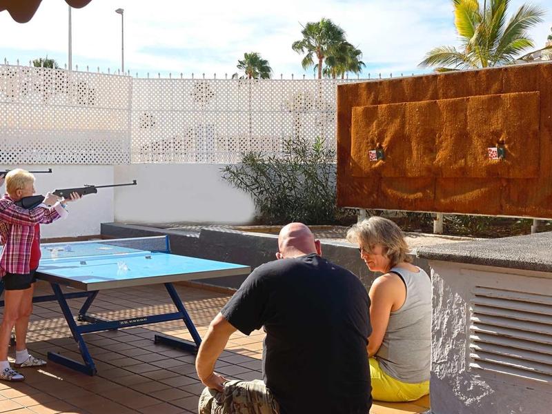 Four people playing outdoor table tennis and two others aiming with air rifles.