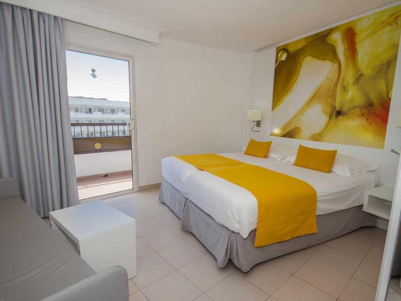 Modern hotel room with double bed, yellow accents, and balcony access with sea view.