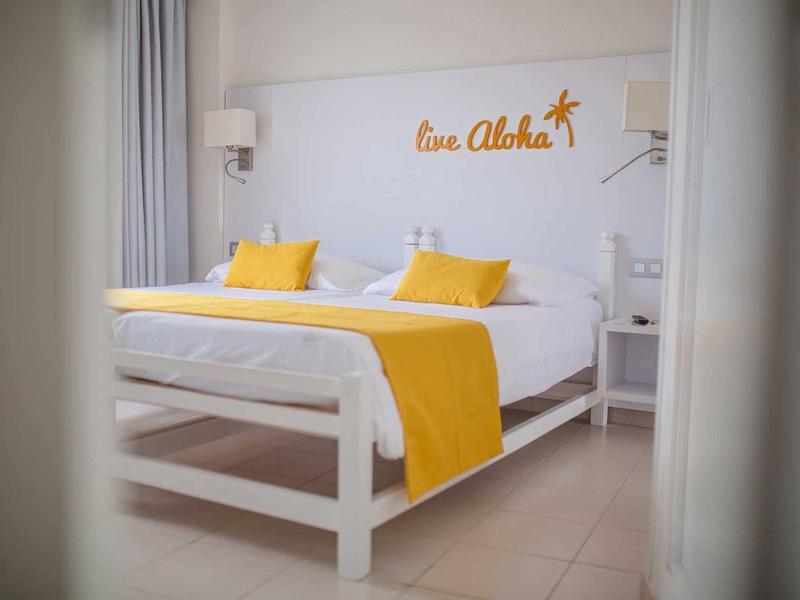 Bright hotel room with large bed, white bedding, and yellow accents.