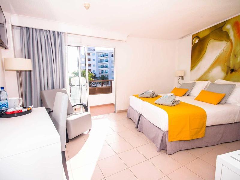 Bright hotel room with large bed, yellow accents, and a balcony.