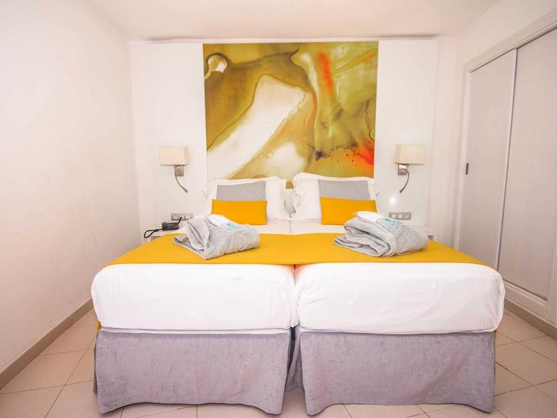 Bright hotel room with two single beds and modern wall art.