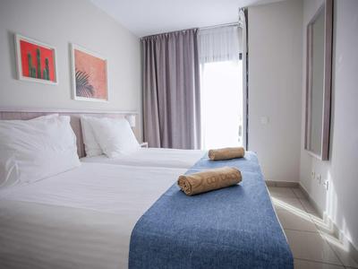 Modernes, helles Schlafzimmer mit zwei weißen Betten, blauen Decken und gerollten Handtüchern.