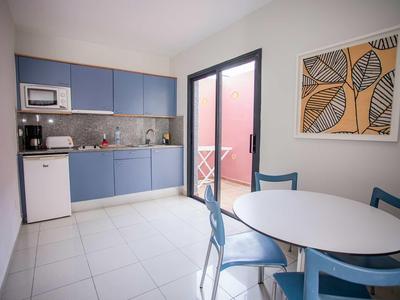 Helle Küche mit blauen Schränken, runder weißer Tisch und blauen Stühlen, großes Fenster, Wandbild.