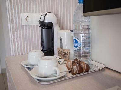 Kaffeepadmaschine, zwei weiße Tassen, Wasserflasche und Kaffeekapseln auf silbernem Tablett.