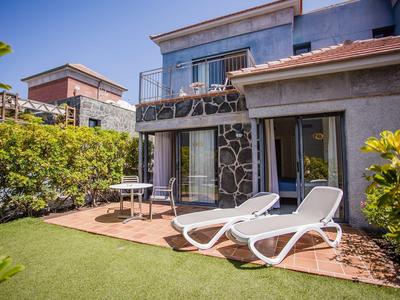 Moderner Garten mit grüner Wiese, zwei weißen Liegestühlen, Tisch mit Stühlen und zweistöckigem Haus.