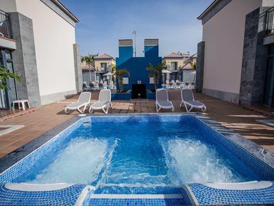 Jacuzzi z niebieskimi płytkami na tarasie między budynkami, z krzesłami w tle.