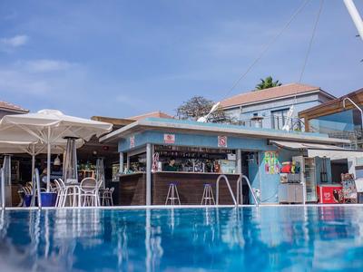 Bar przy basenie z stołkami i stolikami obok basenu pod niebieskim niebem.