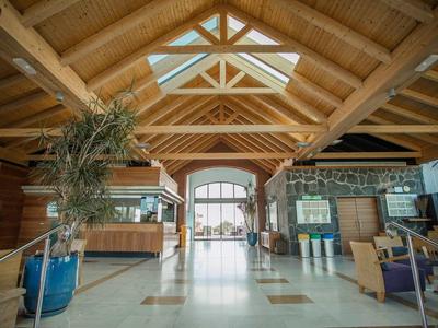 Großes Holzgebäude mit transparentem Dach, Sitzbereich und Pflanzen im Eingangsbereich.