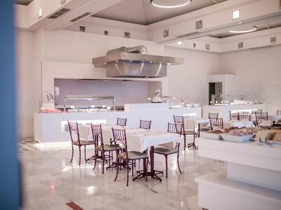 Heller, leerer Gastraum mit weißen Wänden, glänzendem Boden und mehreren Tischen mit Stühlen.