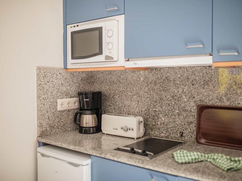 Kleine Küche mit blauen Schränken, Kaffeemaschine, Toaster, Herd und Mikrowelle auf grauer Arbeitsplatte.