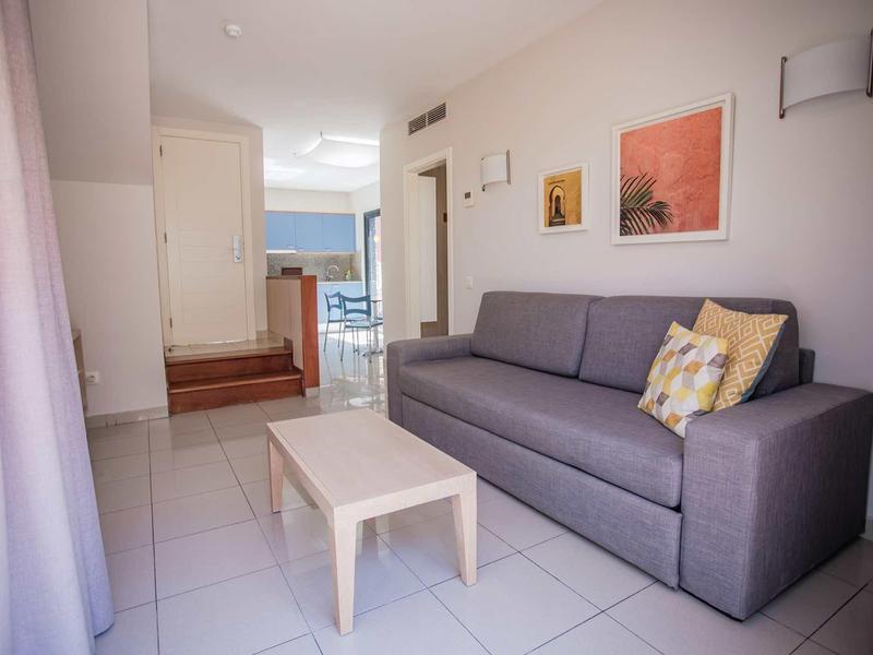 Moderner Wohnraum mit grauem Sofa, kleinem Tisch, heller Fliesenwand und Kunstwerken an der Wand.