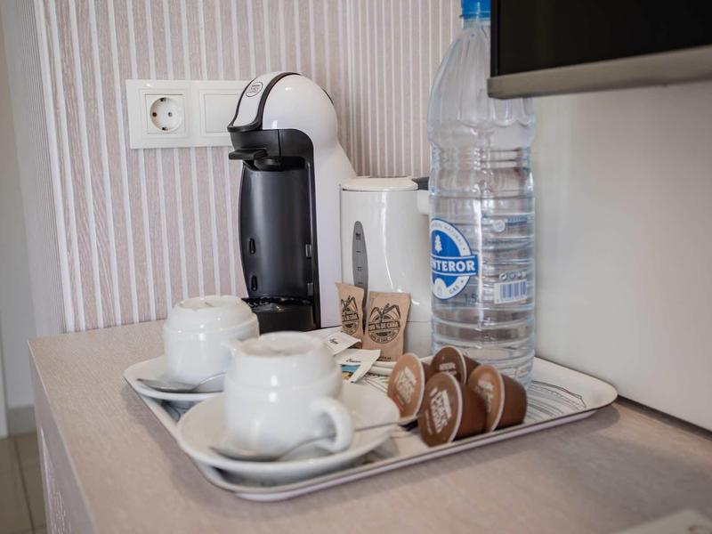 Kaffeepadmaschine, zwei weiße Tassen, Wasserflasche und Kaffeekapseln auf silbernem Tablett.