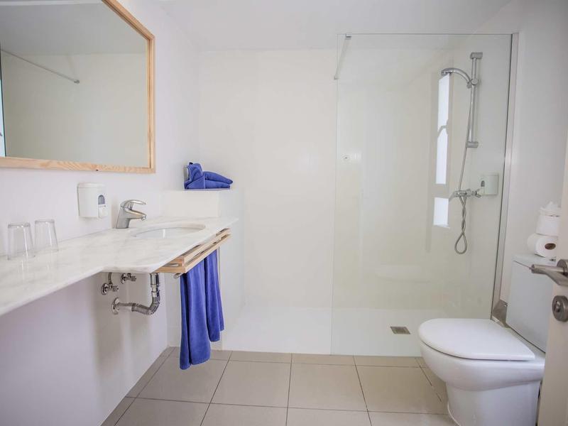 Helles, modernes Badezimmer mit großer Dusche, weißem WC, Waschtisch und blauem Handtuch.